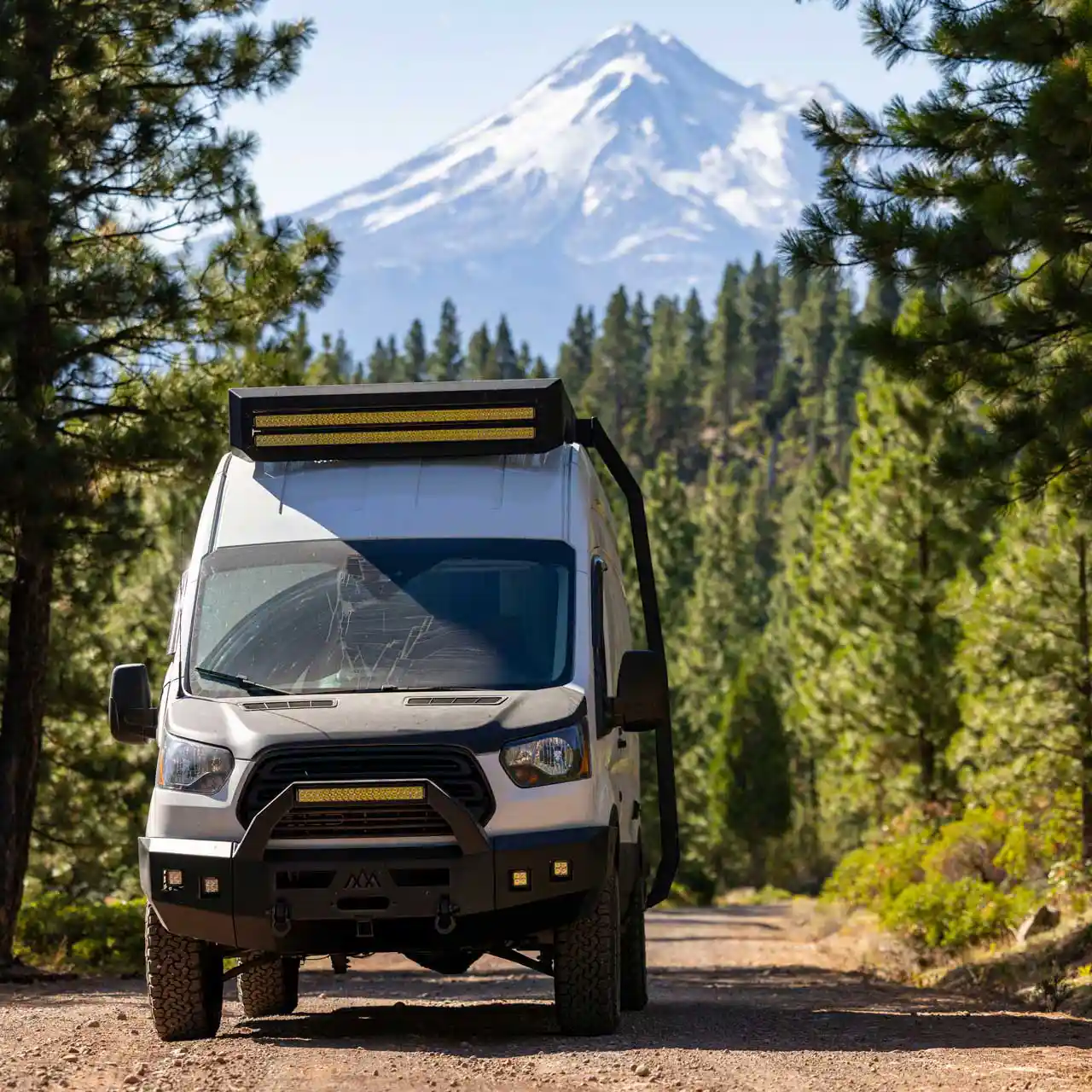 Adventure van in a Pacific Northwest forest with a snow-capped mountain framed between the pines